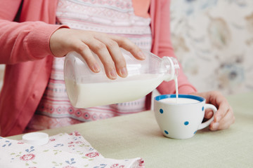 Fototapeta na wymiar Beautiful woman in pink pouring milk into cup, fresh healthy food