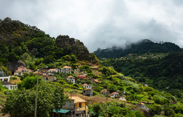 Fototapeta na wymiar Mountain landscape. A small village is located on the mountainside. Green mountains, small cottages, gardens and orchards are depicted. In the background you can see clouds above the mountain tops.