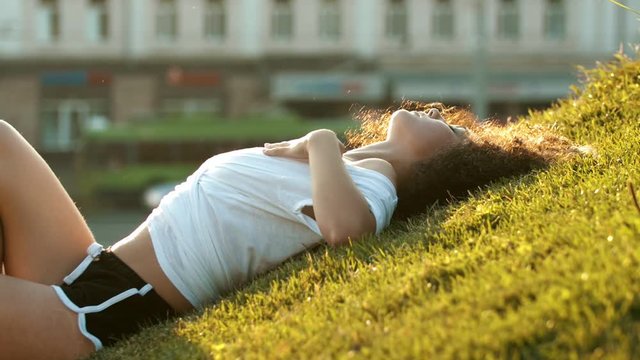 Attractive skinny young woman lying on the grass and hugging herself with her hands - then stand up