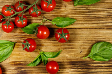 Fresh cherry tomatoes with green basil leaves on a wooden table. Top view