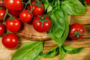 Fresh cherry tomatoes with green basil leaves on a wooden table