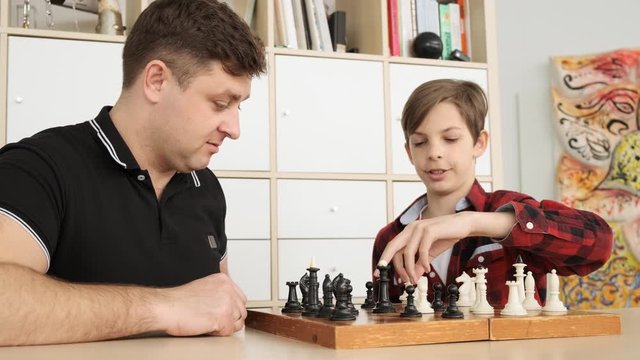 Father and son are playing chess and smiling while spending time together at home slow motion