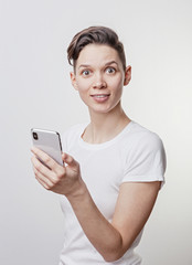 Fototapeta premium Happy funny millennial woman's celebrating win or victory, triumph, holding a phone. Cheerful excited girl, laughing, having fun, using cell phone apps. Isolated on white studio blank background.