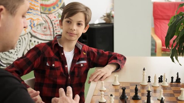 Happy teenage kid is laughing winning his father in chess front view slow motion