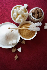 Various types and shapes of sugar on red background with empty space for logo or title. Sugar hearts, clubs diamonds, spades. Stick sugar, cane brown white sugar. Top view