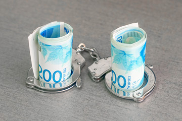 roll Israeli money bills of 200 shekel in handcuffs isolated on gray background. Shekel banknotes...
