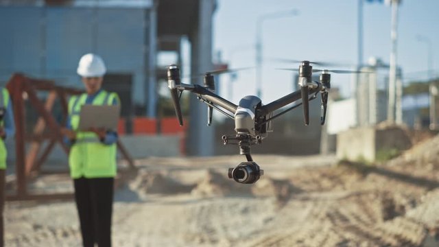 Two Specialists Use Drone on Construction Site. Architectural Engineer, Safety Engineering Inspector Fly Drone on Commercial Building Construction Site Controlling Design and Quality. Focus on Drone