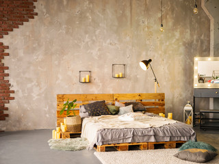 Wooden double bed in elegant bedroom interior with silver painting and black lamp, mirror, candles, colorful pillows. Concept for interior design, bed or home comfort