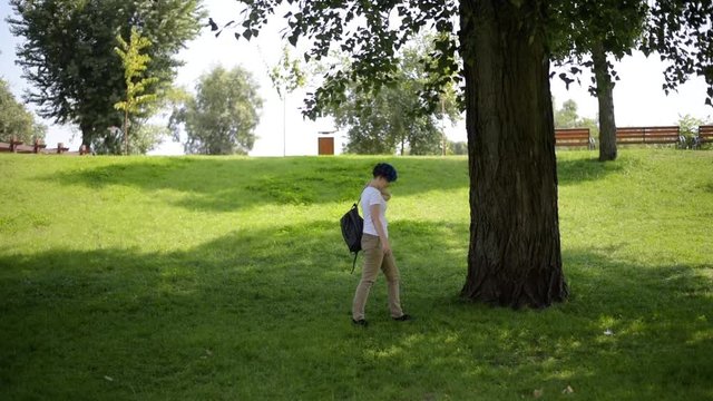 Student girl with backpack goes through park., summer day in city park