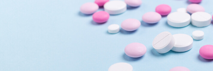 Pink and white tablets on blue background Heap of assorted various medicine tablets Horizontal banner Health care Close-up Copy space