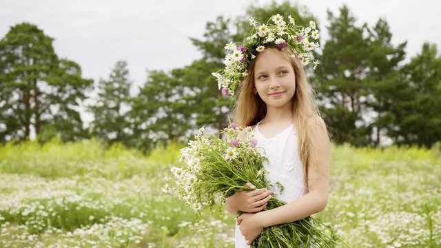 Smiling girl in floral wreath with chamomile bouquet summer field. Portrait girl teenager with flower bouquet posing on camomile field at summer day