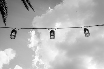 Isolated decorative hanging string lamps lights. Lantern lamps with moody sky background. Palm tree background.