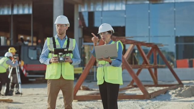 Two Specialists Controlling Drone on Construction Site. Architectural Engineer and Safety Engineering Inspector Fly Drone on Building Construction Site Controlling Quality. Focus on Drone