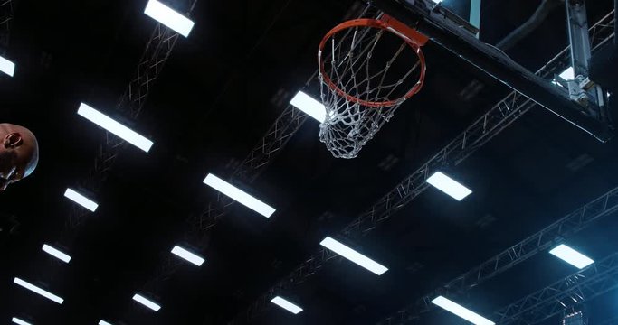 Low angle of professional basketball player in action performing slam dunk in a basketball hoop on a sports arena