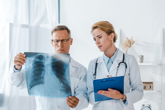 attractive doctor holding clipboard and looking at x-ray near coworker