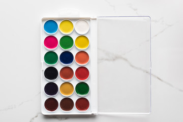 top view of opened watercolor paint palette on marble white surface