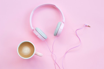 Pink headphones and coffee cup on a pink background. Music concept
