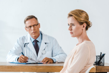 selective focus of upset woman sitting near doctor in white coat