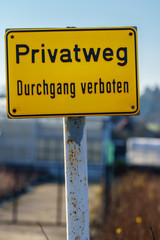 Yellow sign with German text "Private road no trespassing" in front of a house - vertical