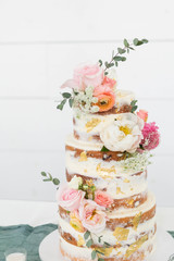 Obraz na płótnie Canvas Naked Wedding Cake Decorated with Gold Foil and Flowers, Three Tiered Cake, White Background, Copy Space