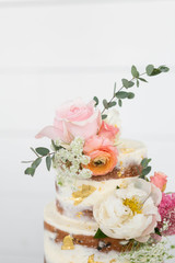 Obraz na płótnie Canvas Top of Naked Wedding Cake Decorated with Gold Foil and Flowers, Three Tiered Cake, White Background, Copy Space