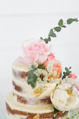 Up Close Naked Wedding Cake Decorated with Gold Foil and Flowers, Three Tiered Cake, White Background, Copy Space