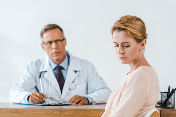 Obraz premium selective focus of sad woman sitting near doctor in white coat