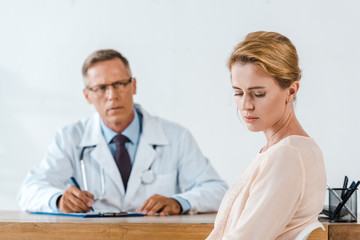 selective focus of sad woman sitting near doctor in white coat
