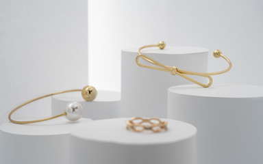Modern golden bracelets and ring on white cylinders setup