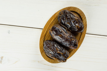 Group of three whole dried brown date medjool on bamboo plate flatlay on white wood