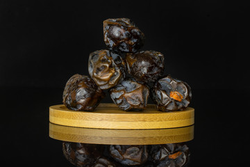 Group of six whole dried brown date medjool on bamboo plate isolated on black glass