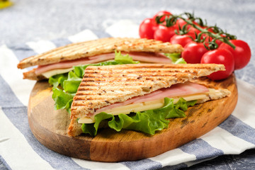 Half of a sandwich in the form of a triangle on a wooden board. The sandwich is decorated with a lettuce leaf and cherry tomatoes.