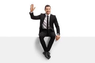 Young man in a suit sitting on a panel and waving at the camera