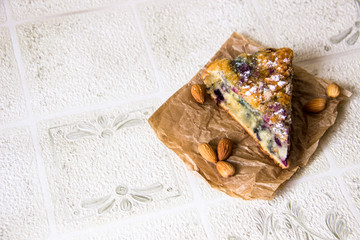 Close-up the slice of cake with berries and almonds decorated with powdered sugar on a brown paper napkin. Almonds lie next to the cut piece of cake. Homemade bakery cake. Delicious breakfast dessert.