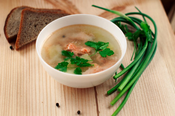 Hot healthy trout fish soup with greens and potatoes in a white bowl on a wooden table on a Sunny day