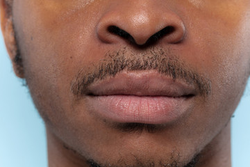Close up portrait of young african-american man on blue background. Human emotions, facial expression, ad, sales or men's beauty and health concept. Photoshot of lips. Looks calm.