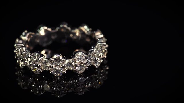 Platinum wedding ring with shining diamonds on black mirror background.
