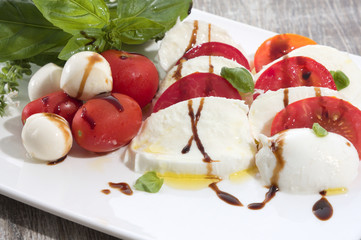 Tomate mozarella mit basilikum olivenöl und aceto balsamico auf weissem teller auf holz