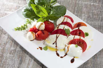 Tomate mozarella mit basilikum olivenöl und aceto balsamico auf weissem teller auf holz