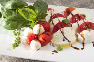 Tomate mozarella mit basilikum olivenöl und aceto balsamico auf weissem teller auf holz