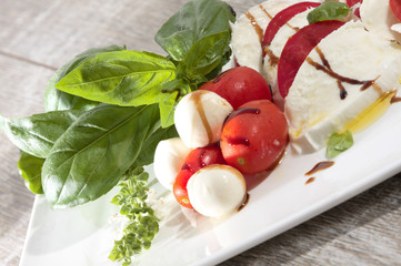 Tomate mozarella mit basilikum olivenöl und aceto balsamico auf weissem teller auf holz
