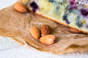 Close-up the almonds lie next to the cut piece of cake on a brown paper, macro. Almond nuts as ingredients for baking. Healthy food. Delicious breakfast or dessert. Vegetarian food.