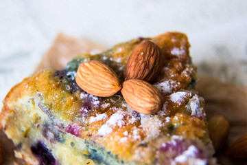 Close-up the almonds lie on the slice of cake with berries decorated with powdered sugar, macro. Homemade bakery cake. Almond nuts as ingredients for baking. Healthy food. Delicious breakfast dessert.