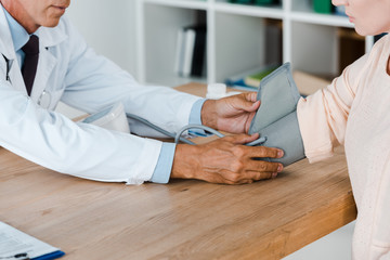 cropped view of doctor measuring blood pressure of woman on table in hospital
