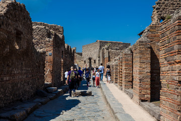 Tourists at the streets of Pompeii made of large blocks of black volcanic rocks