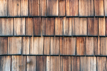 Weathered and faded from the sun wooden shingles that are the facade of an alpine house. Wooden texture in shades of gray and orange.