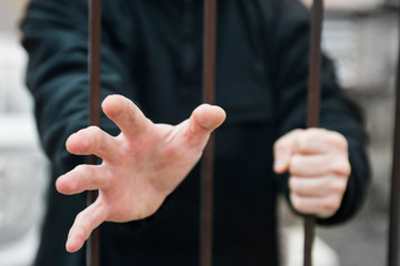 Man's hand stretches through the bars locked man in a cage cell. Hand of a refugee behind fence