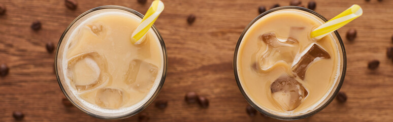 selective focus of ice coffee with straws in glasses and coffee grains on wooden table, panoramic shot