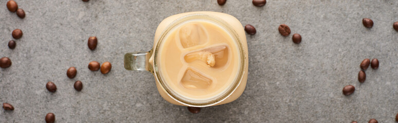top view of ice coffee in glass jar near coffee grains on grey background, panoramic shot