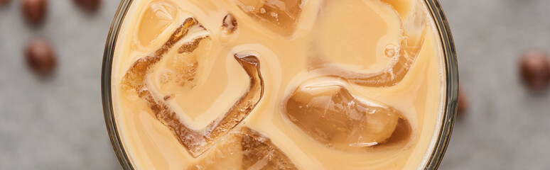 close up view of ice coffee in glass with straw and coffee grains on grey background, panoramic shot